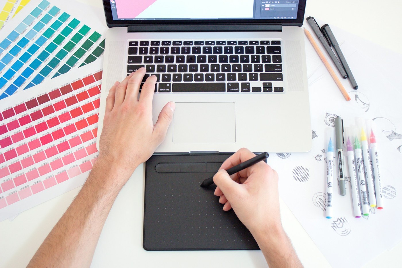 Designer working on a laptop with a drawing tablet and color swatches, representing building Amazon A+ Content for product listings